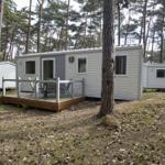 Wohnwagen mit Terrasse im Wald. Holzdecke, Stühle und Tische sind vorhanden.
