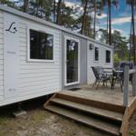 Wohnwagen mit Terrasse und Sitzgruppe im Wald. Holzterrasse mit Tisch und Stühlen.