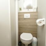 Badezimmer mit Toilette, WC-Behälter und Fenster. Auf dem Fensterbrett steht eine Pflanze.