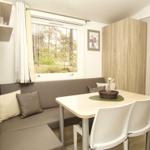 Essbereich mit Sitzbank, Tisch und Stühlen. Fenster zeigt Wald. Schrank und Wandregal sichtbar.