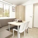 Essbereich mit Sitzbank, Tisch und Stühlen. Fenster zeigt Wald. Hintergrund: Schrank und Türen.