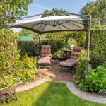 Garden with sunshade, two lounge chairs, and flower beds on stone paving.