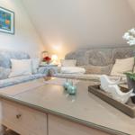 Living room with comfortable sofas, glass table, and flower decoration under sloped ceiling.