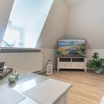 Living room with TV, plants, and skylight. Wooden floor and white cabinet.
