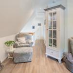 Living area with armchair, sofa, and glass cabinet. Wooden floor and sloped ceiling.
