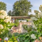 House with thatched roof, surrounded by flowers and stone walls in the garden.