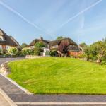 House with thatched roof, large lawn, and paved path.