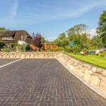 Paved courtyard with stone wall, lawn, and traditional houses with thatched roofs.