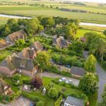 Village with thatched houses and green gardens beside a river.