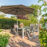 Terrace with table, chairs, and umbrella. Surrounded by flowers and hedge.