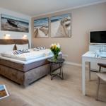 Bedroom with bed, table, and TV. Wall art depicts beach landscapes.