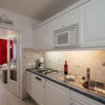 Kitchen with white cabinets, sink, and microwave. Corridor to living area with red curtains.