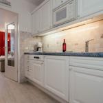 Kitchen with white cabinets, countertop, and view into living room with red curtains.