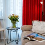 A sofa with cushions and an open book, next to a chair and table with flowers.
