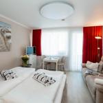Room with sleeping area, sofa, dining table, and window with red curtains.