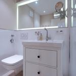 Bathroom with sink, mirror, and toilet. Shelves are above the mirror.