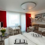 A bedroom with bed, sofa, dining table, and window with red curtains.