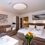 Bedroom with sofa, bed, and kitchen area. Wall paintings show coastal landscapes.