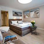 Bedroom with bed, TV, and table. Wall art shows beach landscapes.
