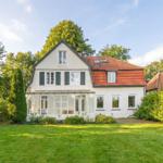 House with red roof and green garden. Glass veranda and windows visible.