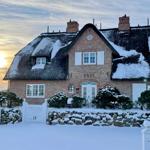 Schneelandschaft vor einem traditionellen Haus mit Strohdach und Backsteinfassade.