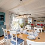 Esszimmer mit Tisch, Stühlen und blauem Sideboard. Im Hintergrund Wohnbereich mit Sofa und Stehlampe.