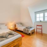 Zimmer mit zwei Betten, Holzboden und Fenster. Ein roter Stuhl steht daneben.