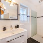 Badezimmer mit Dusche, Waschbecken und Spiegel. Fenster mit Vorhang.