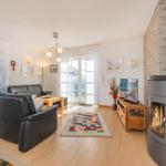 Wohnzimmer mit Sofa, Kamin und TV. Holzboden und große Fenster.
