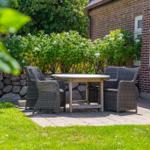 Patio with table and chairs in front of a brick house with flower hedge.