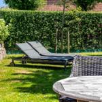 Garden with sun loungers, table and chairs. Backyard with hedge and stone wall.