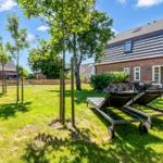 House with garden, sun loungers, and terrace. Lawn and trees visible.