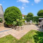 Garden with paving, green areas, seating, and stone wall.