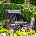 Garden with beach chair, table, and chair. Background: hedge and roses.