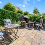 Terrace with garden furniture, grill, and plants in the background.
