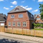Red brick building with wooden fence and green lawn under a blue sky.