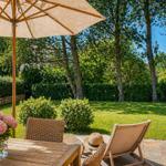 Terrasse mit Tisch, Stuhl und Sonnenschirm. Grünflächen und Bäume im Hintergrund.