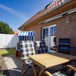 Terrasse mit Tisch, Stühlen, Grill und Strandkorb. Hinterhof mit Rasen und weißer Wand.
