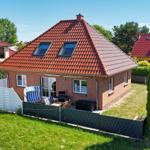 Ein Haus mit rotem Ziegeldach und Garten. Außenterrasse mit Sitzgelegenheit.