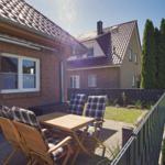 Terrasse mit Holztisch, Stühlen und Grill. Hinterhof mit Rasen und Zaun.