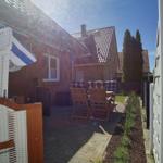 Terrasse mit Holzstühlen und Tisch. Weiße Wicker-Struktur. Hinterhof mit Beete und Zaun.