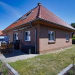 Ein Haus mit rotem Dach und Backsteinfassade. Gartenbereich mit Grill und Sitzgelegenheit.