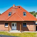 Ein Haus mit rotem Ziegeldach, weißer Tür und grünem Rasen vorne.