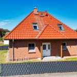 Ein Haus mit rotem Dach und Backsteinfassade. Vorderseite mit weißer Tür und Fenstern.