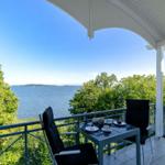 Terrasse mit Tisch und zwei Stühlen bietet Blick auf See und Bäume.
