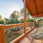 Terrasse mit Holzgeländer und Sitzgelegenheiten. Blick auf grüne Landschaft und Bäume.