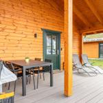 Terrasse mit Tisch, Stühlen und Liegestühlen an Holzhaus mit grüner Tür.