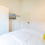 Schlafzimmer mit weißem Bett, gelbem Kissen, weißen Türen und Wandbild.