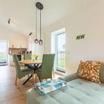 Wohn- und Essbereich mit Sofa, Tisch und Stühlen. Fenster mit Blick auf die Landschaft.