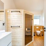 Badezimmer mit Holzsauna, Waschbecken und WC. Holzfußboden und Fenster.